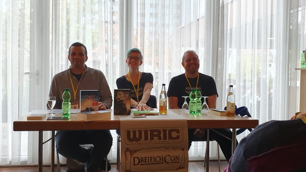 Lesung auf dem BuCon, drei Personen an einem Tisch präsentieren ihre Bücher, von links James Sullivan, Judith Vogt und Christian Vogt